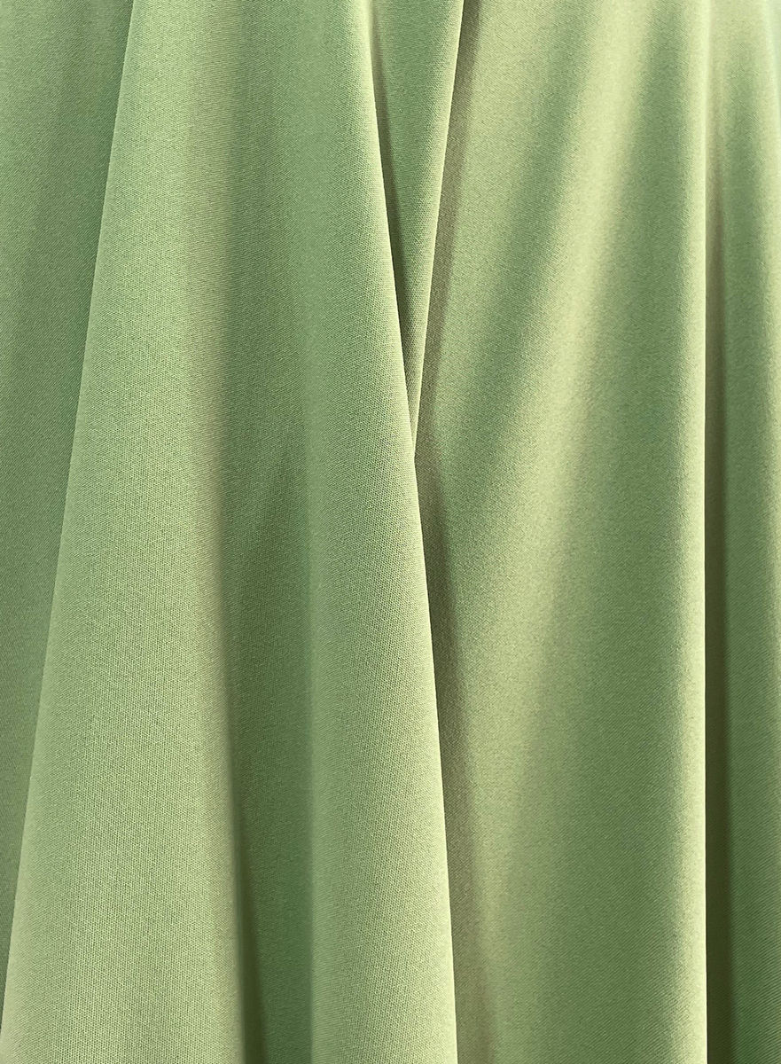 Close-up of pistachio-green fabric with soft folds gathered around a circular fabric-covered detail.