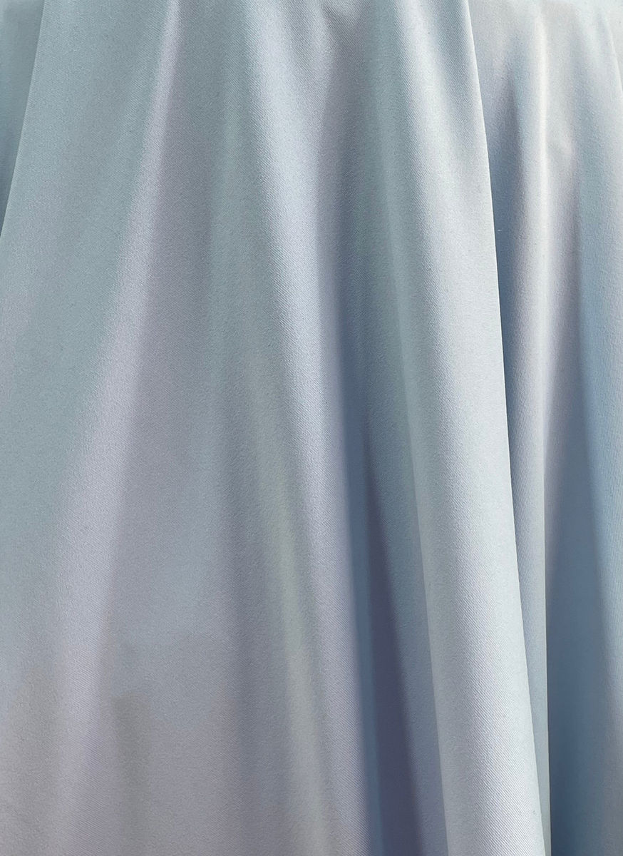 Close-up of light powder-blue fabric arranged in vertical folds highlighting its soft drape and smooth surface.
