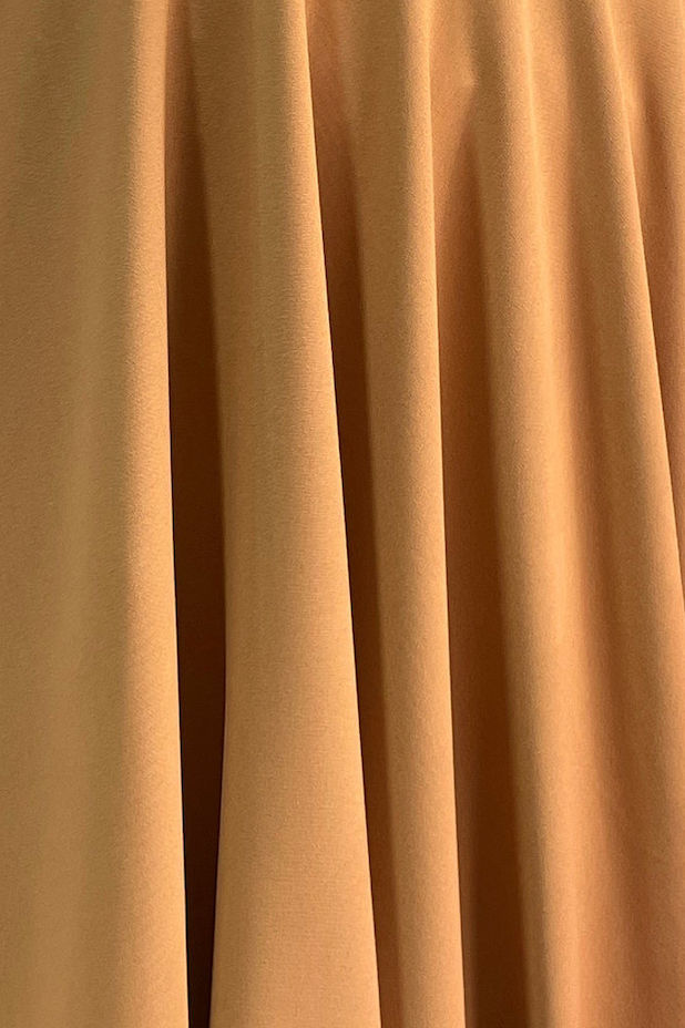 Close-up of warm golden fabric with soft vertical folds showing its drape and texture.